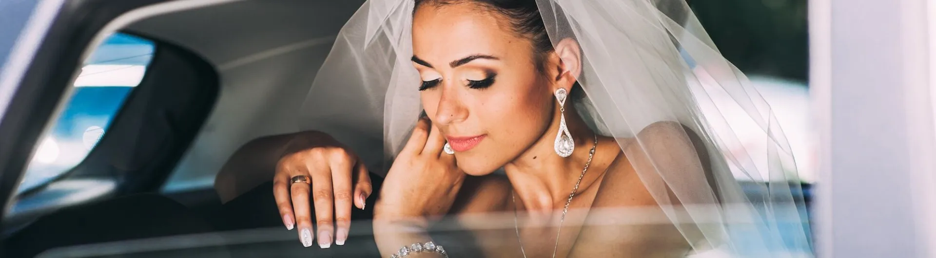 Wedding-Limousine-Service-Hamden-CT-1920w Bride in a wedding dress and veil sits in a car, touching her face gently, with eyes closed and an expression of calm.