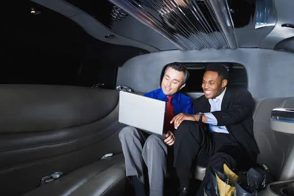 branford-airport-transportation-2880w Two men in business attire are sitting in a limousine, looking at a laptop and smiling.