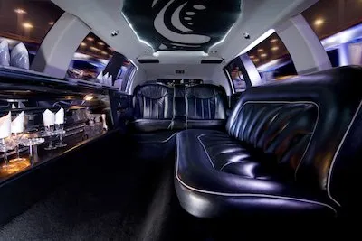 limo-rental-company-near-me-1920w Elegant limo interior with plush black leather seating, ambient lighting, and a stocked bar on the side.