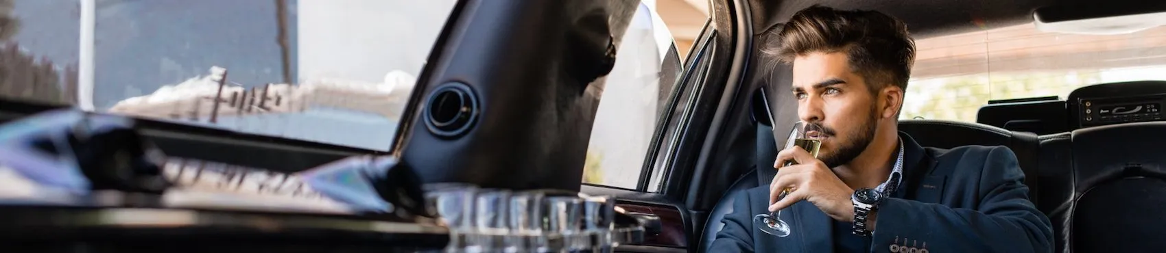 limousine-rental-company-hamden-ct-1920w A man in a suit sits in a car, holding a glass and gazing out the window.