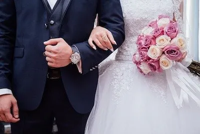 wedding-1920w A bride and groom stand arm in arm; the bride holds a bouquet of pink and white roses.